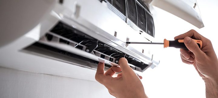 A hand with screwdriver securing the screw lock of the air conditioning unit cover