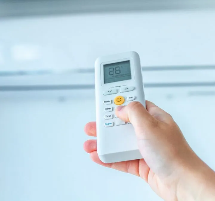 A hand holding an air conditioning remote control to regulate the temperature